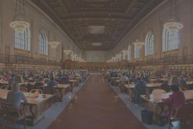 Large library room with rows of tables and chairs and wide arched windows