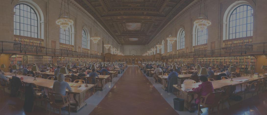 Large library room with rows of tables and chairs and wide arched windows